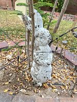 full view of weathered white cement rabbit statue among plants