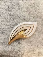front view of stylized leaf brooch showing gold-tone and white enamel detail