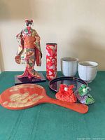 Entire lot showing kimono doll, two tea bowls, kaleidoscope, two small fabric dolls, lacquered tray and hand mirror