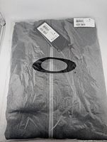 Front view of sealed Oakley grey hoodie in original polybag with tags visible