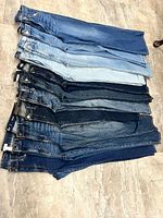 Stack of 11 pairs of women’s jeans laid flat showing front waistbands and various washes