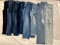 Eleven pairs denim jeans arranged side by side showing varying washes and distressing