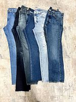 Six pairs of jeans laid flat showing front legs and partial waistbands
