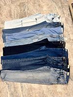 All nine pairs of size 27 jeans laid flat, stacked to show waistbands and washes