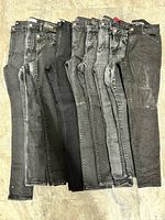 Front view of nine pairs black and grey women’s jeans laid flat