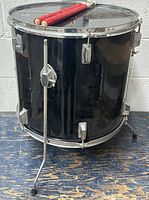 Black floor tom drum on three chrome legs with red mallets resting on top