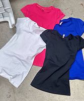 Four sample Sweet N Kool women’s blank T-shirts in white, pink, black, and blue displayed on floor