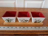 Front view of three ceramic bowls on wooden tray showing winter foliage pattern