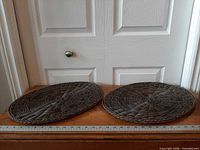 Both oval woven placemats side by side on table with ruler for scale