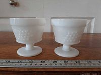 Two Anchor Hocking milk glass sherbet dishes side view with pedestal bases and grape pattern visible