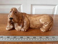 Front left view of brown ceramic basset hound figurine with ruler for scale