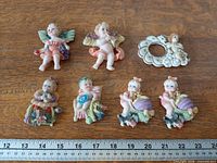 All eight cherub magnets on wood surface with ruler for scale