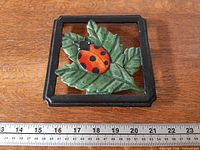Top view of square cast iron trivet with ladybug and leaf design