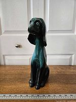 Front view of seated Green/Black drip glaze Blue Mountain Pottery dog figurine with ruler for scale
