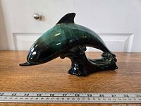Left side view of green and black drip-glazed ceramic dolphin figurine with ruler for scale