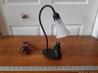 Full view of lamp showing cherub base, curved neck, lily shade and cord next to ruler for scale