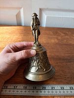 Full view of brass bell beside ruler showing height