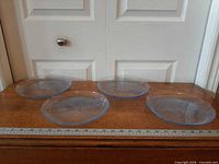 Four blue glass dinner plates on wooden surface with ruler showing scale