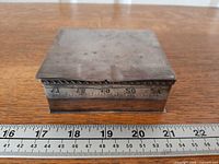 front view of closed silver-plated box beside ruler