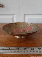 Side profile of brass enamel floral dish showing pedestal base and ruler for scale
