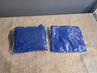 Two sealed blue ponchos in clear plastic sleeves, front view