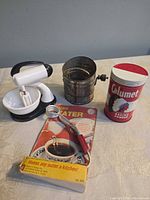Front view showing Calumet tin, flour sifter, immersion heater with packaging and stand mixer