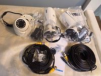 All cameras and accessories laid out: two bullet cameras, one dome camera, BNC cables, power adapters, manuals