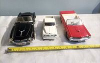 Front view of the three diecast cars side by side on table with measuring tape
