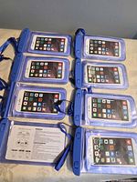 Eight blue waterproof phone pouches laid out front view with sample phones inserted