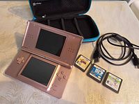 Pink Nintendo DS Lite open with case, cable and game cartridges visible