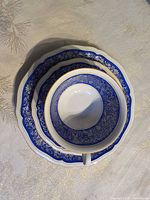 Stacked teacup, saucer and dessert plate showing blue filigree pattern