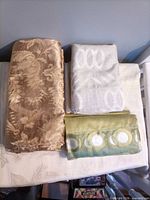 Gold damask, silver geometric, green ring curtain panels folded on table