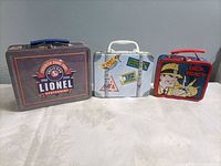Front view of all three tins standing closed showing graphics and handles