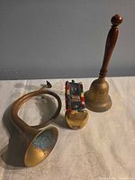 All three items grouped: coiled bugle, cowbell with strap, handbell