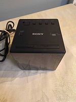 Top view showing Sony logo, snooze/brightness bar, control buttons, and attached AC cord