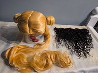 Blonde wig on stand with long wavy tails beside black curly extension