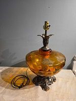 Full view of amber glass table lamp showing glass body, metal base, socket and cord