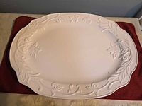 Front view of large white porcelain platter with embossed floral scroll border