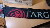 Unboxed scarf showing red dragon sigil and partial "TARG" lettering on black knit