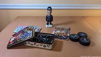 Overall view of bobblehead, pucks, pencils, packaged set, tin