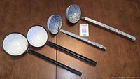 Four ladles laid on table showing bowl interiors and speckled exteriors