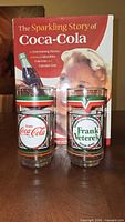 Front view of two Frank Vetere's Coca-Cola glasses in front of book