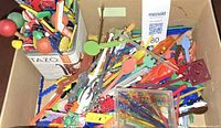 Cardboard box holding bulk of multicolour plastic stir sticks and picks along with metal Tazo tin and clear plastic case