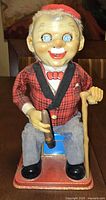 Front view of tin toy showing old man seated on trunk with cigar and cane