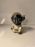Full view of black and silver baby Buddha figurine seated with peace sign