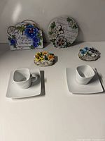 Lot overview showing two white square cup-and-saucer sets and four ceramic plaques
