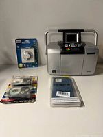 Group shot of Epson PictureMate printer, Philips timer package, Casio tape pack, blue phone case