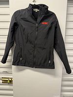 Front view of black Port Authority soft shell jacket hanging, full garment visible