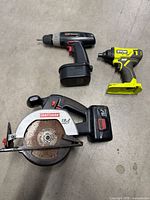 Three cordless power tools laid out: Craftsman circular saw with battery, Coleman drill, Ryobi impact driver