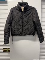 Front view of black quilted coat hanging